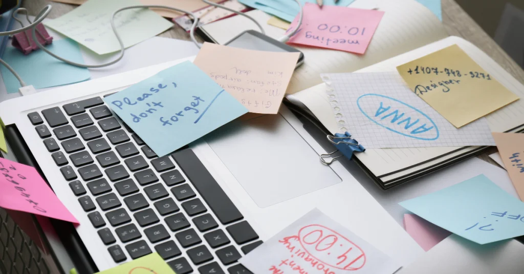 Messy desk with sticky notes and scattered papers representing the disorganization job seekers face without a Job Application Tracker.