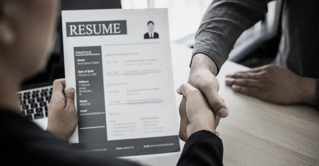 Job candidate handing resume to recruiter, how ATS applicant tracking system affects resume success during hiring.