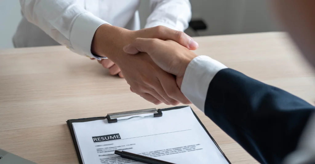 Job interview questions and answers – successful interview handshake with resume on the table.