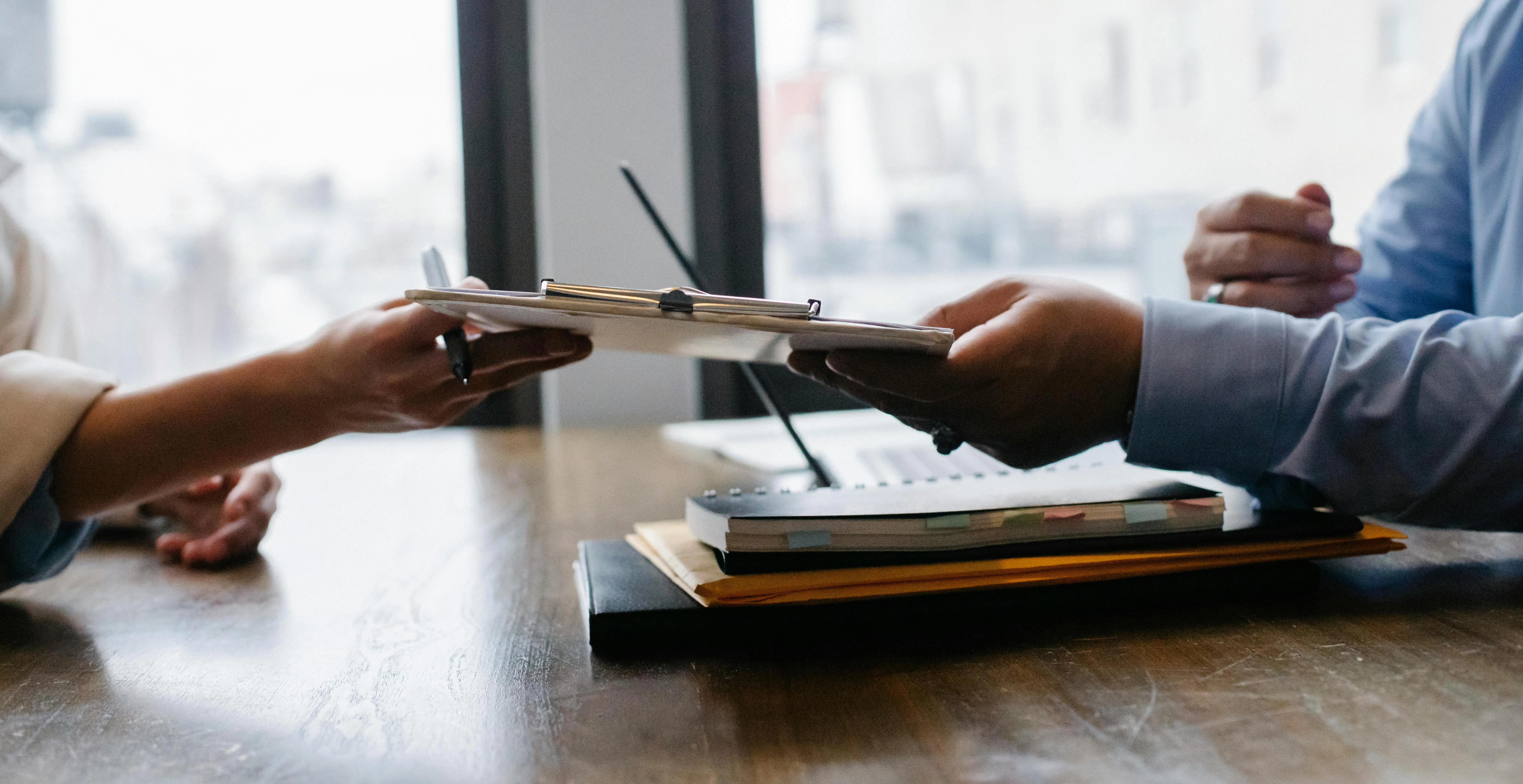 A job seeker handing a resume to a hiring manager across a desk during an interview

